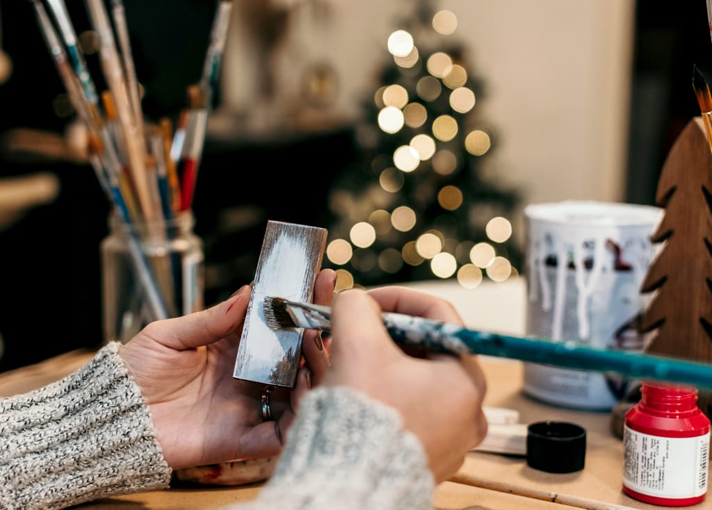 A female hand painting a wood stick on a blurred Christmas tree background