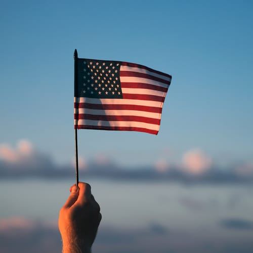 Hombre sosteniendo una bandera estadounidense ante la puesta del sol. Concepto relacionado con el Día de la Independencia o con viajar por Estados Unidos.